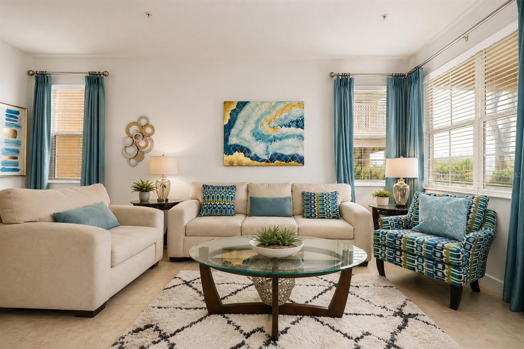 A living room features a beige sofa, patterned armchair, glass coffee table, and blue curtains — 894 ASSEMBLY COURT, REUNION, FL