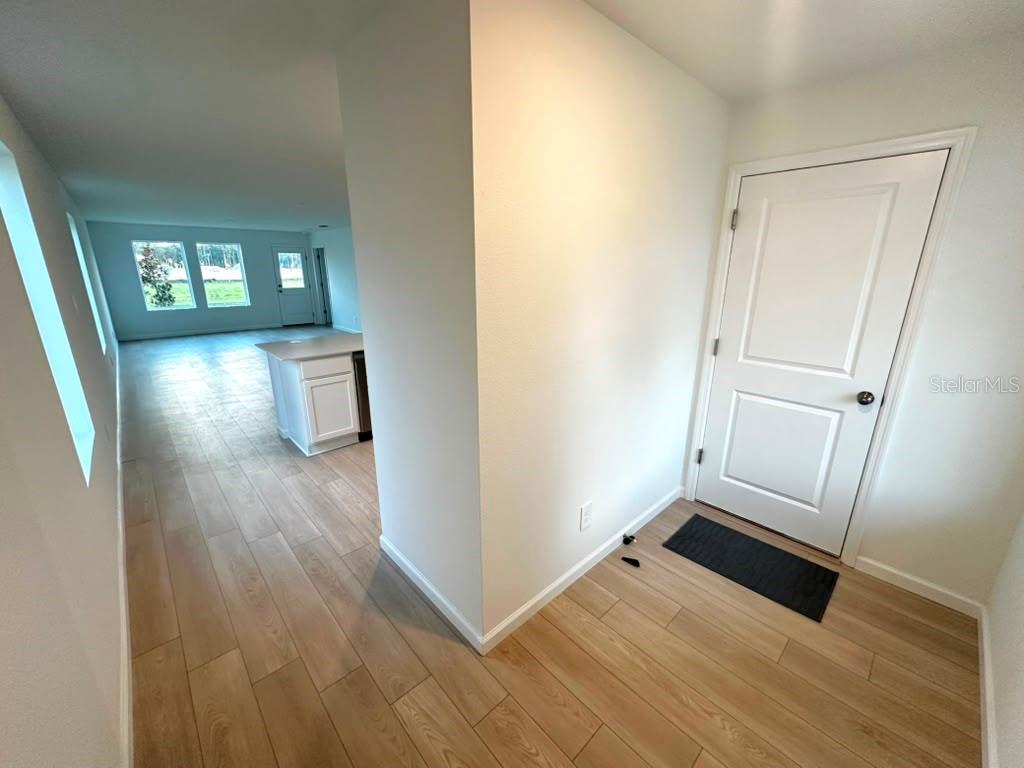 An entryway with light wood-look tile flooring leads into an open-concept kitchen and living area — 5608 MORANT BAY PATH, KISSIMMEE, FL