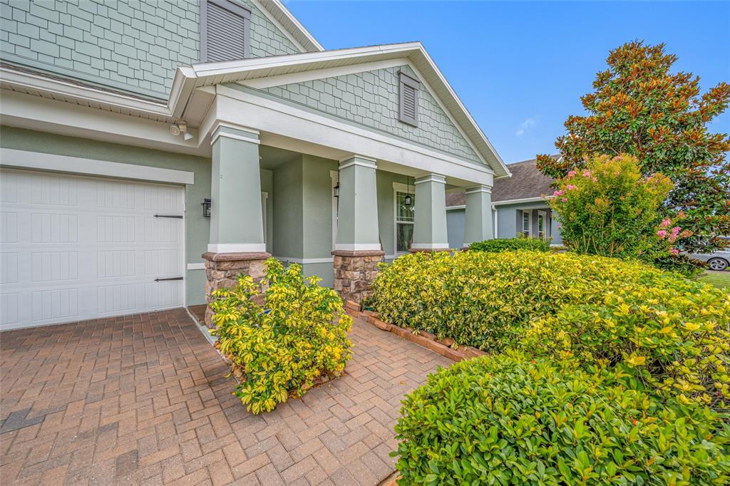 A light green house exterior features a paved walkway, stone-based columns, and manicured landscaping — 19382 LONG LAKE RANCH BOULEVARD, LUTZ, FL