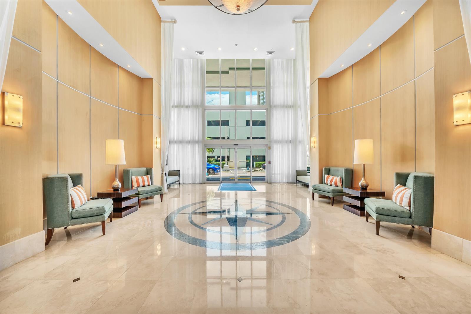 A spacious lobby features a compass rose floor inlay, tall windows, and symmetrical seating areas — 1945 S Ocean Drive # 1803, Hallandale Beach FL 33009, HALLANDALE BEACH, FL