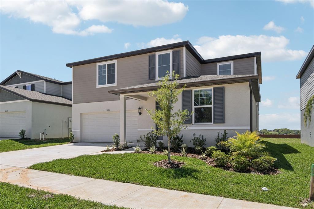 A two-story suburban house with a beige stucco lower level and gray siding upper level — 12581 HOMELAND DRIVE, DADE CITY, FL