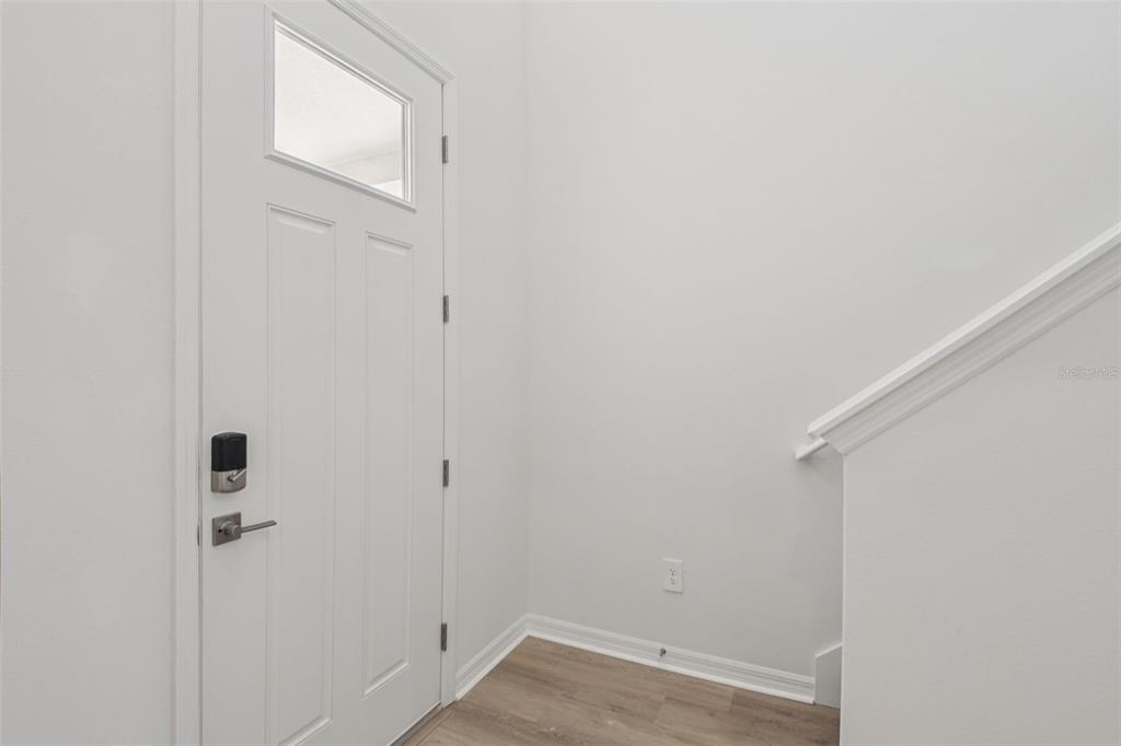 A white front door with a smart lock opens into an entryway with wood-look flooring — 12581 HOMELAND DRIVE, DADE CITY, FL