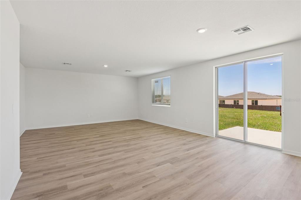 An empty living room features light wood-look flooring, white walls, and a sliding glass door — 12581 HOMELAND DRIVE, DADE CITY, FL