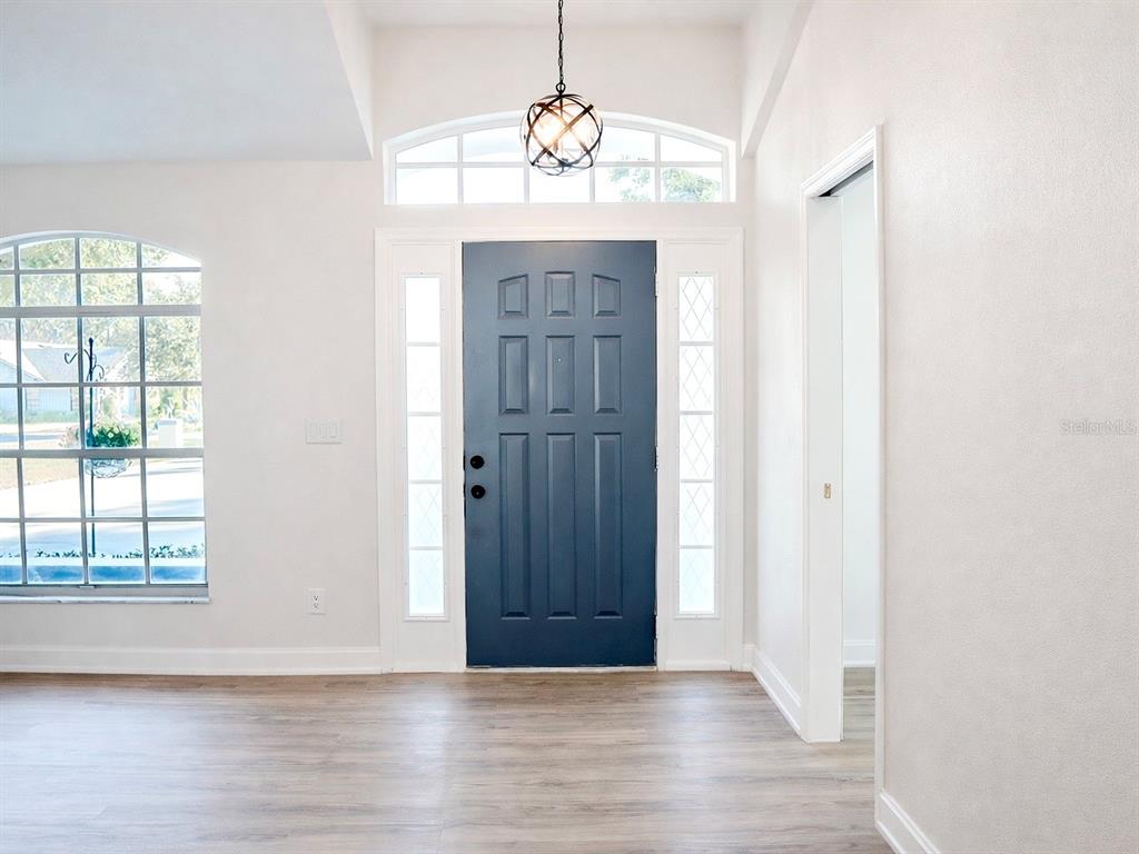 An entryway features a blue front door, sidelights, a transom window, and wood-look flooring — 10711 LAKE HILL DRIVE, CLERMONT, FL