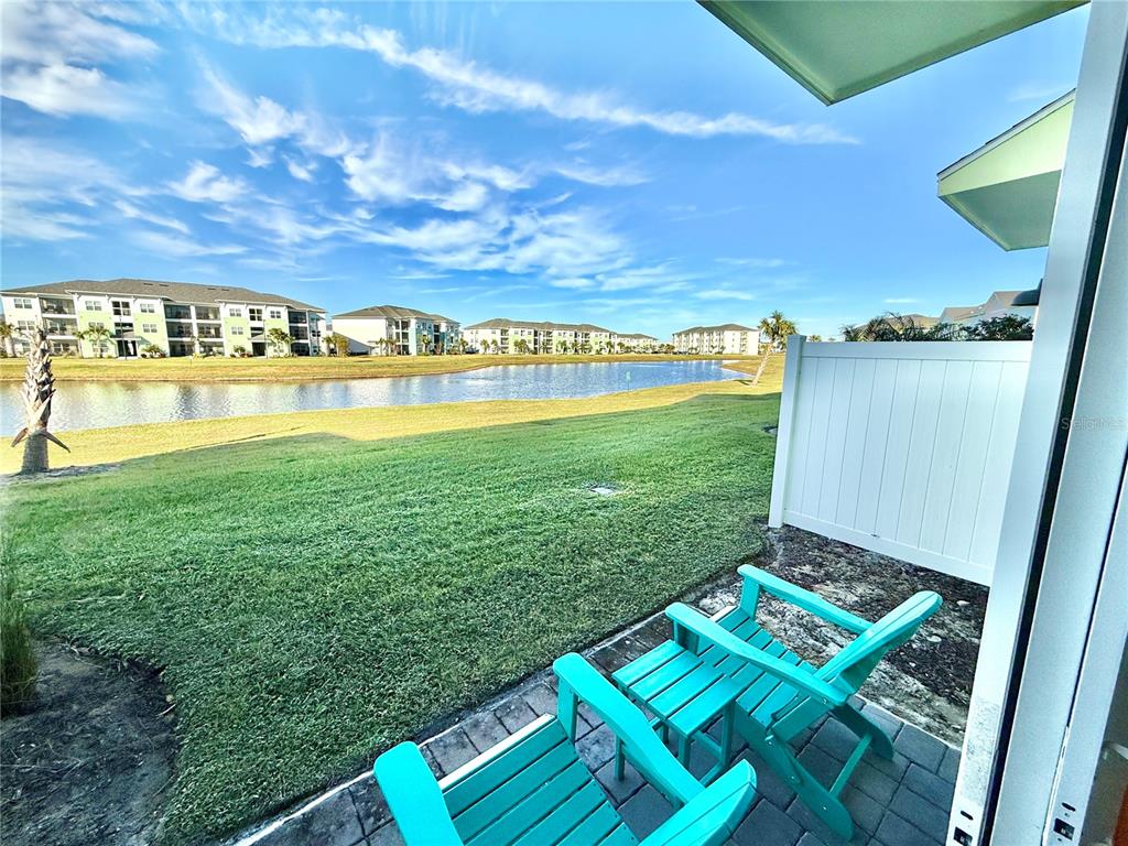 A patio with two turquoise chairs overlooks a grassy lawn and a pond — 3165 CARIBBEAN SOUL DRIVE, KISSIMMEE, FL