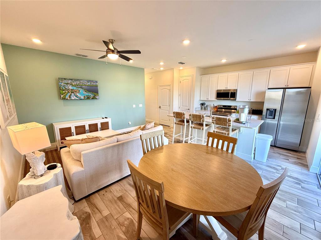 An open-concept living and dining area features a light green accent wall and wood-look flooring — 3165 CARIBBEAN SOUL DRIVE, KISSIMMEE, FL