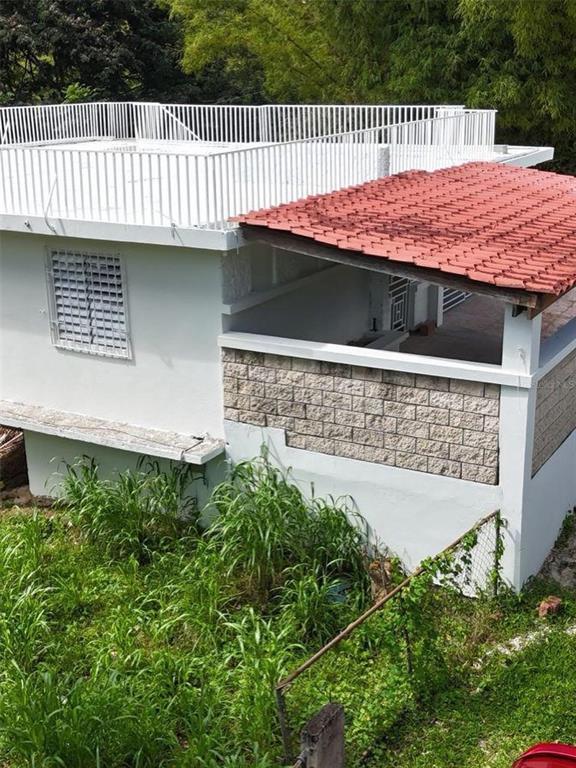 A white house with a flat roof, a red-tiled porch, and a stone-textured exterior wall — PR 7790 Juan Asencio JUAN ASENCIO, AGUAS BUENAS, PR