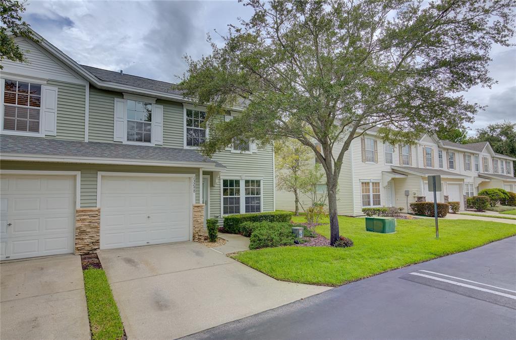 A two-story townhouse with light green siding, a white garage door, and a paved driveway — 13298 THOROUGHBRED LOOP, LARGO, FL