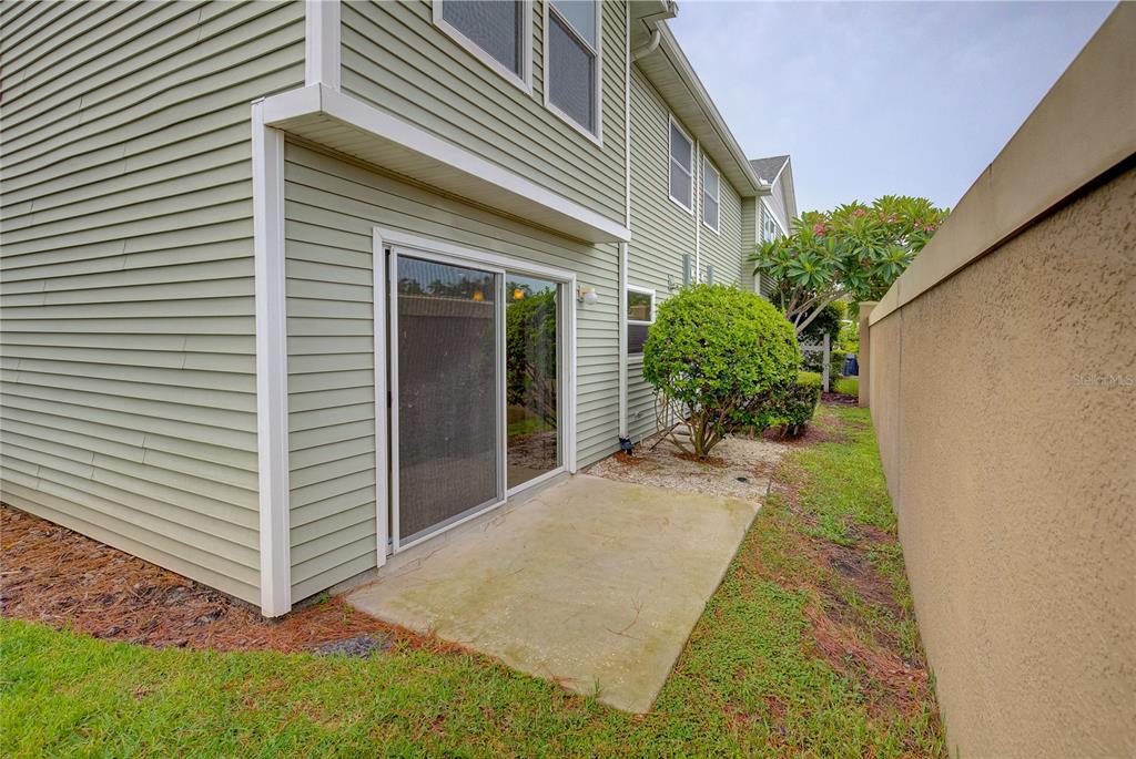 A light green vinyl-sided house exterior features a concrete patio and a sliding glass door — 13298 THOROUGHBRED LOOP, LARGO, FL