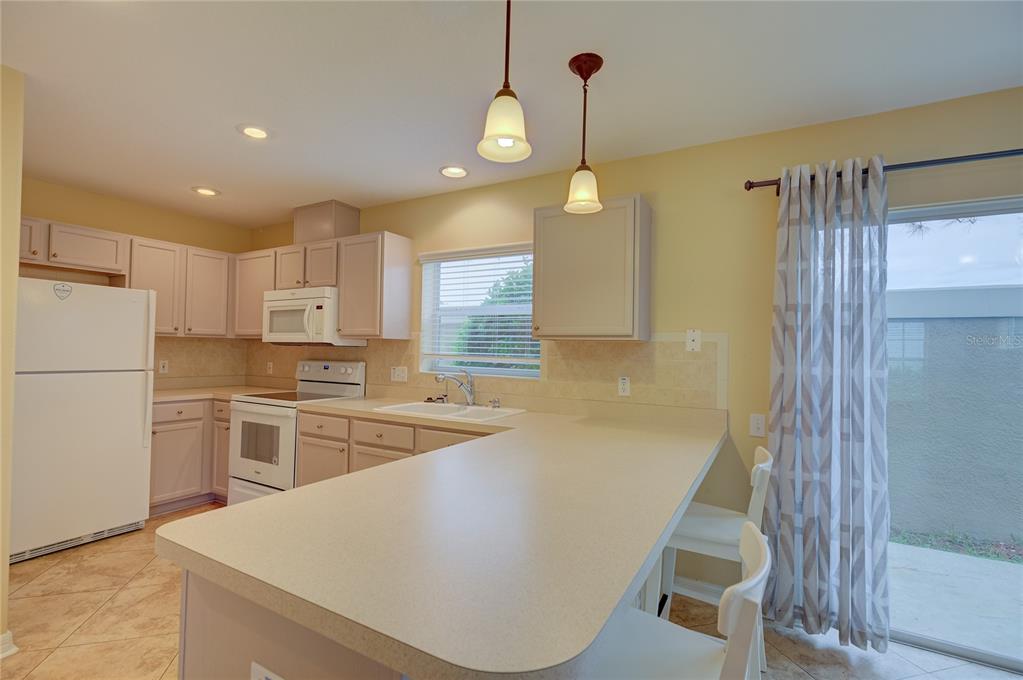 A kitchen with light-colored cabinets, white appliances, a breakfast bar, and a sliding glass door — 13298 THOROUGHBRED LOOP, LARGO, FL