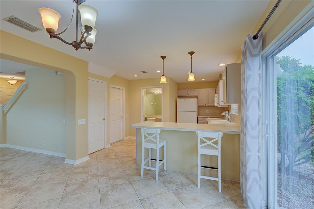 A kitchen with a breakfast bar, white stools, tile flooring, and a sliding glass door — 13298 THOROUGHBRED LOOP, LARGO, FL