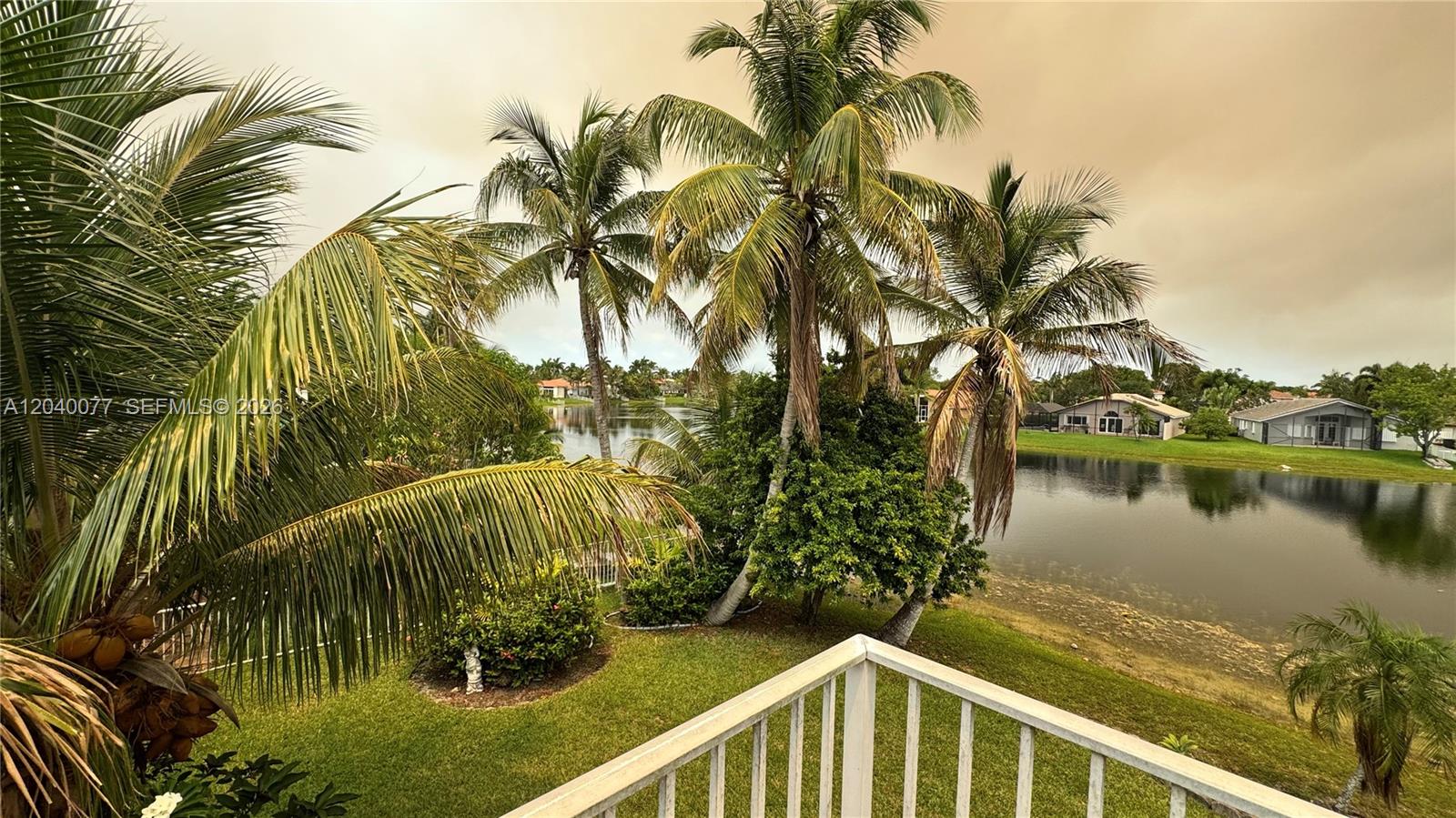 A view from a balcony overlooking a grassy yard, palm trees, and a lake — 17471 SW 12th St, Pembroke Pines FL 33029, PEMBROKE PINES, FL