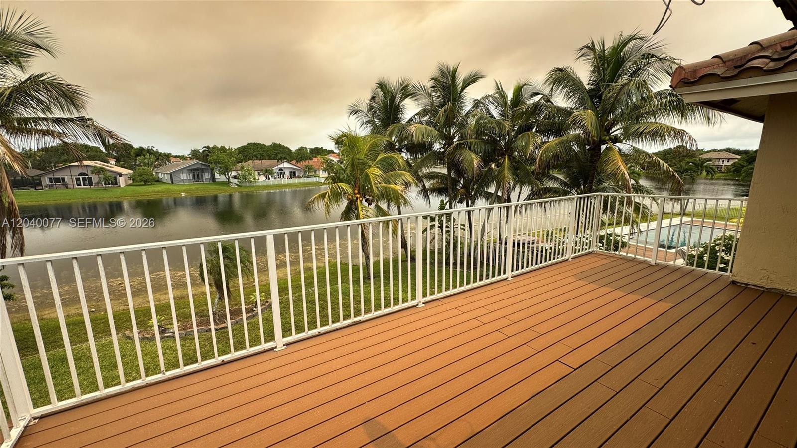 An elevated wooden deck features a white railing overlooking a lake and palm trees — 17471 SW 12th St, Pembroke Pines FL 33029, PEMBROKE PINES, FL
