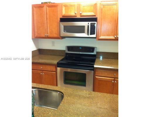 A kitchen features wood cabinets, dark countertops, stainless steel appliances, and tile flooring — 13147 SW 42nd St # 6103, Miramar FL 33027, MIRAMAR, FL