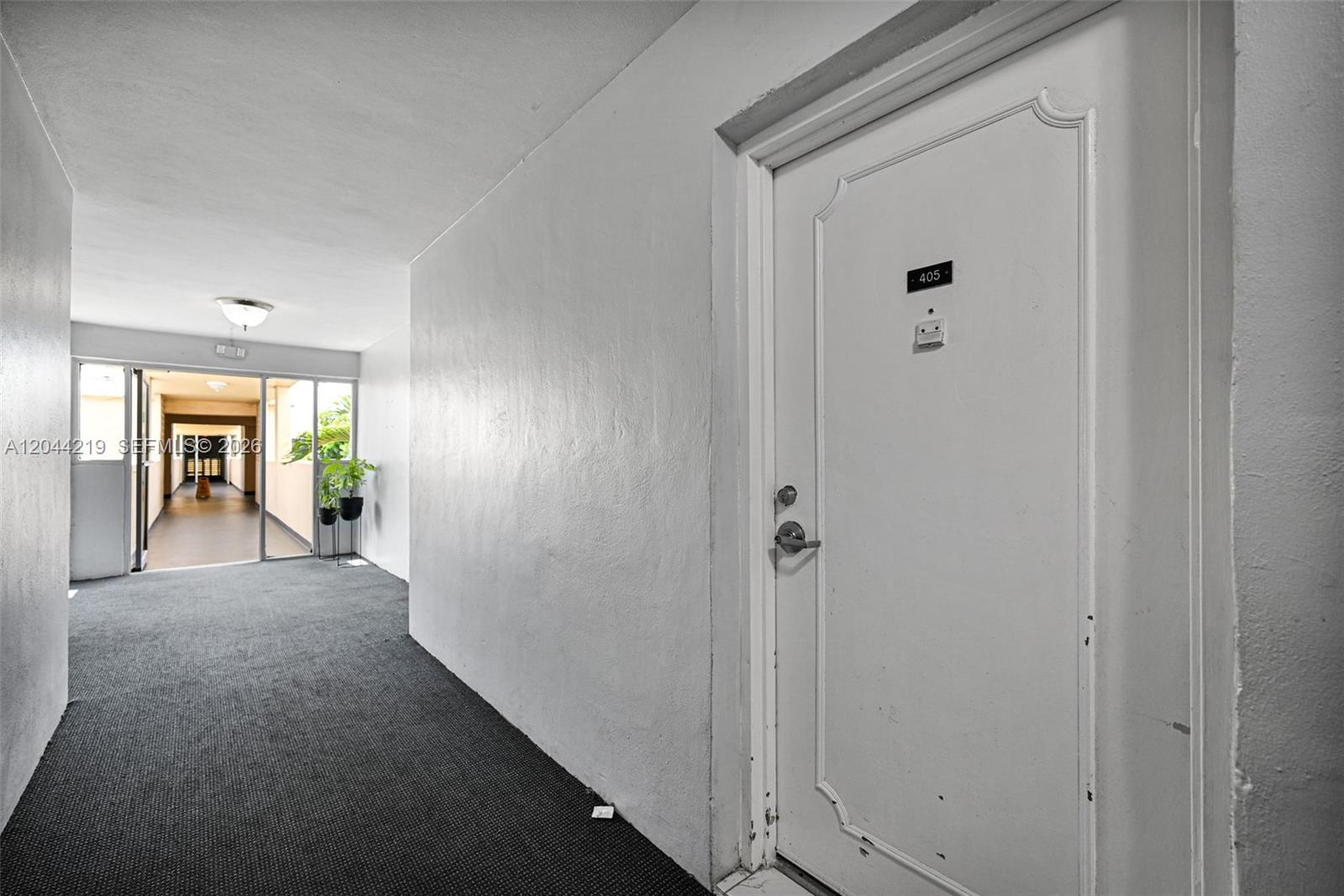 A hallway with gray carpeting leads to a white door labeled 405 — 942 NE 199th St # 4E, Miami FL 33179, MIAMI, FL