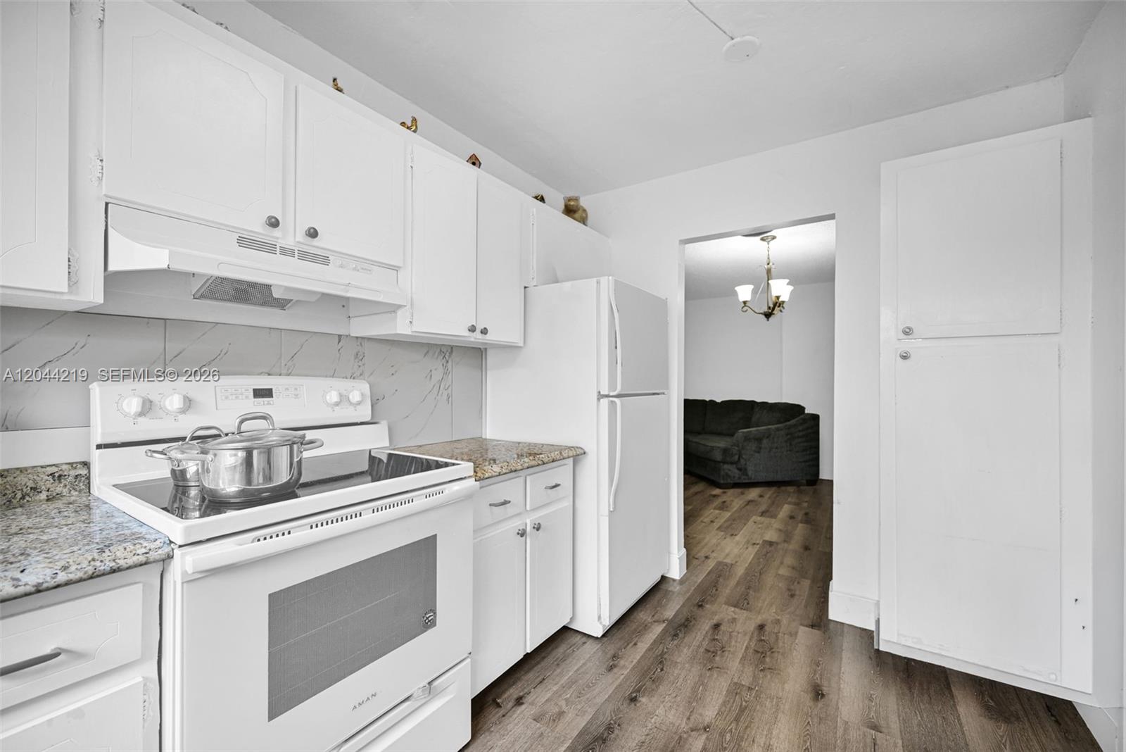A white kitchen features granite countertops, white cabinetry, and stainless steel appliances — 942 NE 199th St # 4E, Miami FL 33179, MIAMI, FL