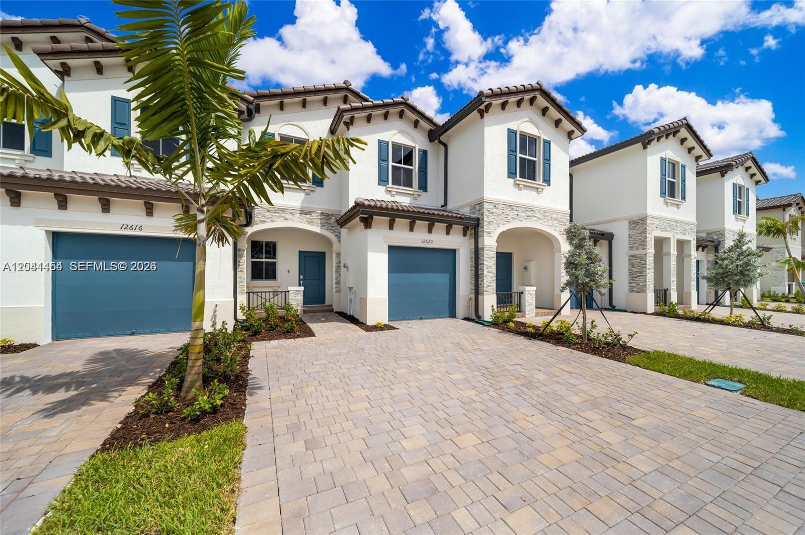 A row of two-story townhouses features stucco exteriors, blue garage doors, and paver driveways — 12620 NW 23rd Pl, Miami FL 33167, MIAMI, FL