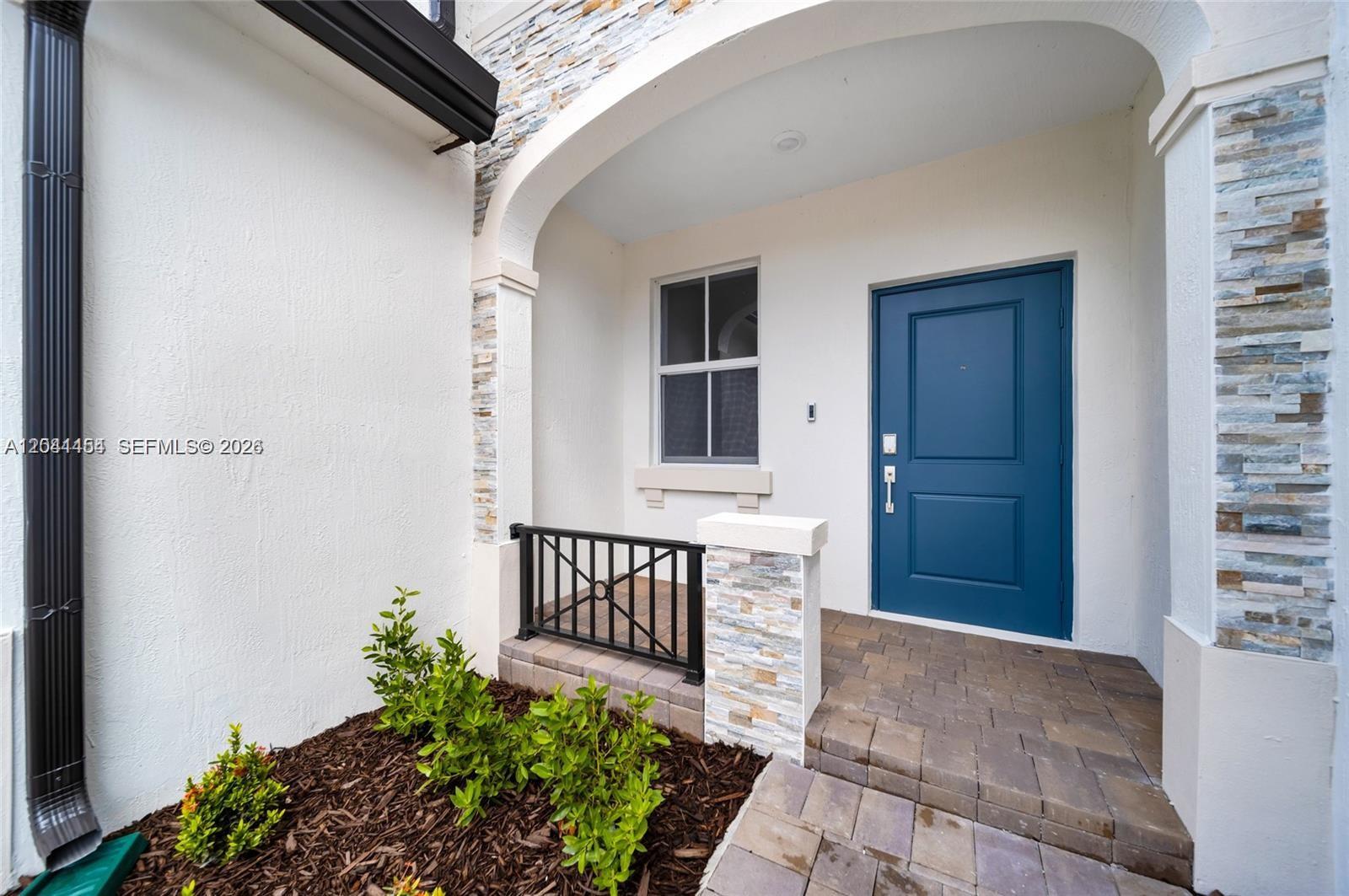 A blue front door is set within a covered entryway featuring stone accents and pavers — 12620 NW 23rd Pl, Miami FL 33167, MIAMI, FL