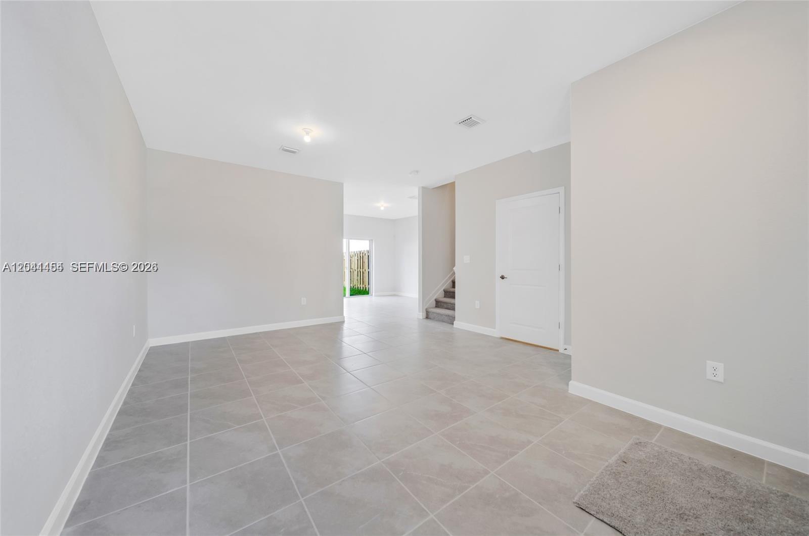 An empty room features light gray tile flooring, white walls, a closed door, and stairs — 12620 NW 23rd Pl, Miami FL 33167, MIAMI, FL
