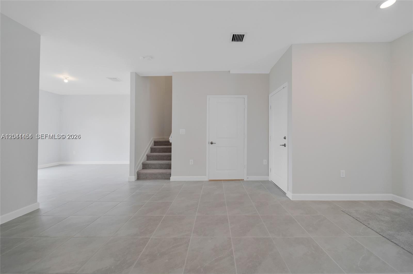 A room with gray tile flooring, a carpeted staircase, and two white doors — 12620 NW 23rd Pl, Miami FL 33167, MIAMI, FL