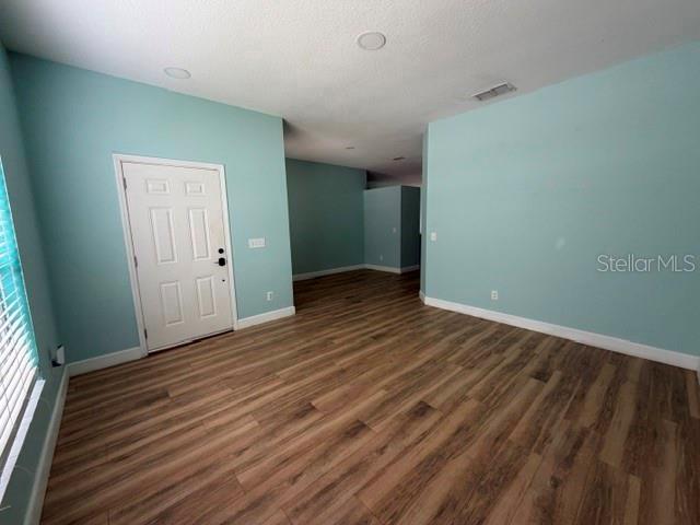 An empty room features light blue walls, wood-look flooring, and a white front door — 10640 SUN VILLA BOULEVARD, ORLANDO, FL