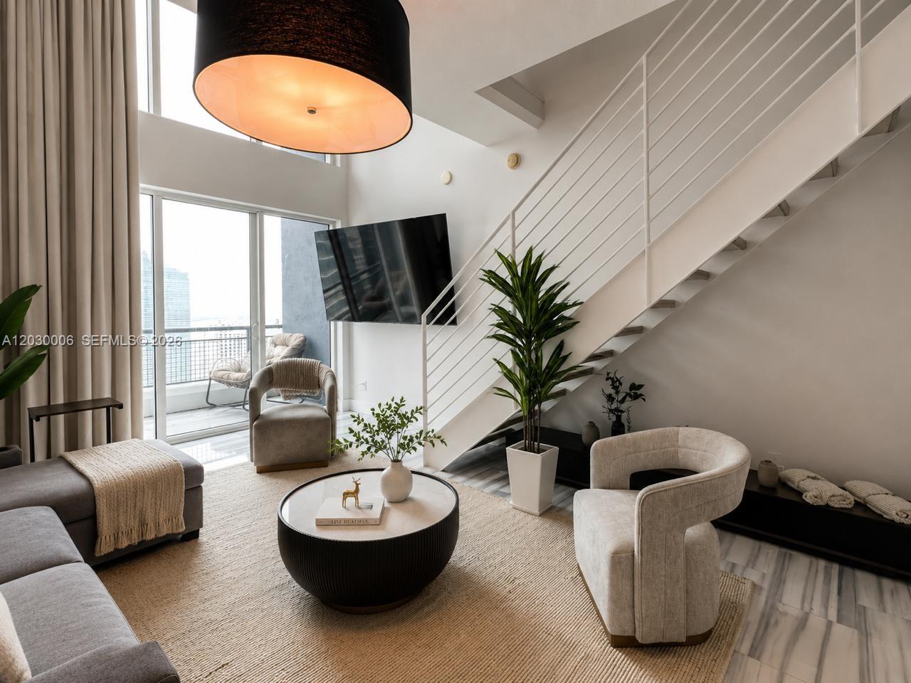 A modern living room features a floating staircase, a large pendant light, and floor-to-ceiling windows — 60 SW 13th St # 3004, Miami FL 33130, MIAMI, FL