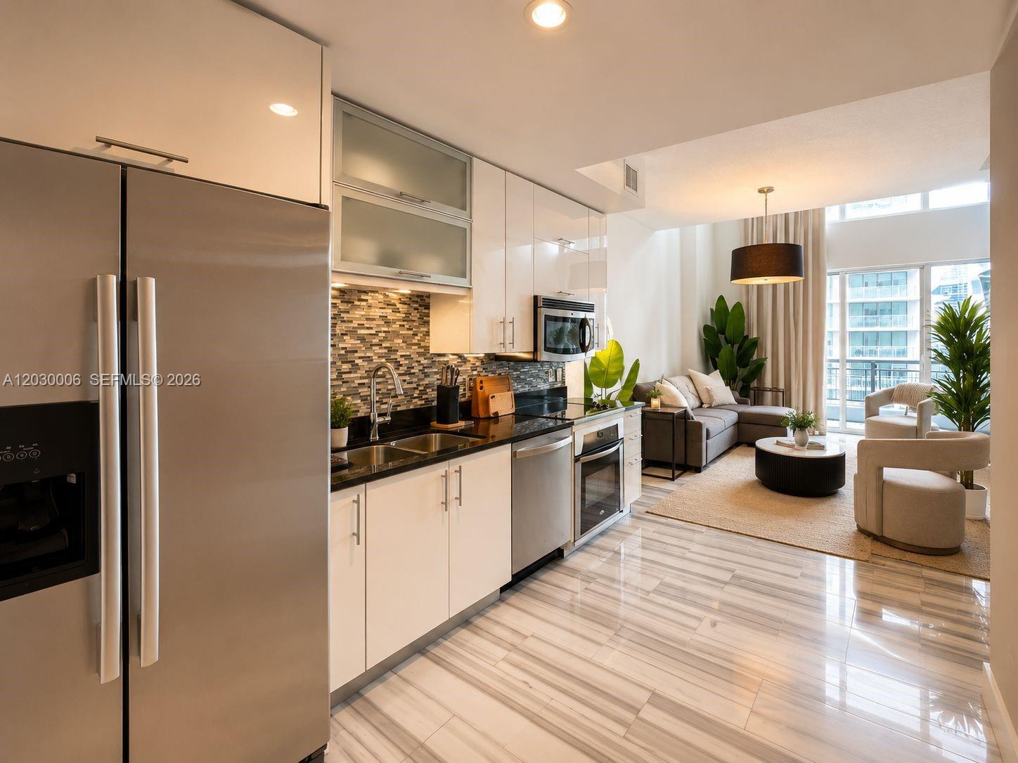 A modern kitchen with stainless steel appliances and white cabinets opens into a living area — 60 SW 13th St # 3004, Miami FL 33130, MIAMI, FL