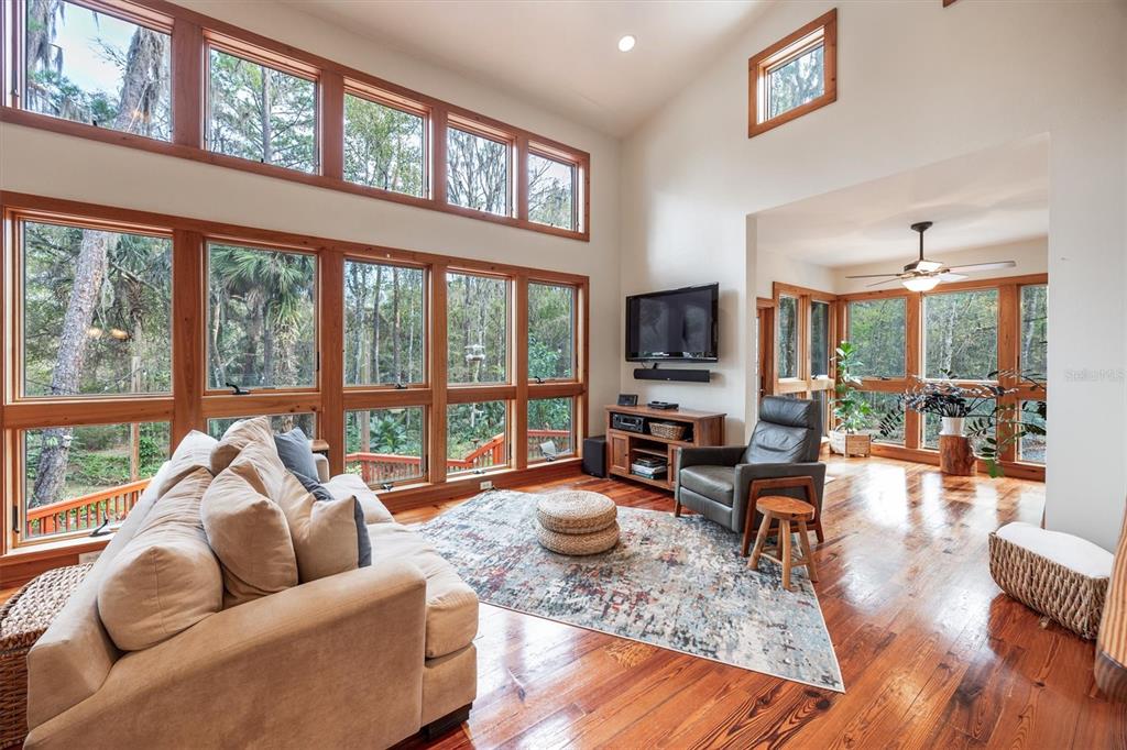 A living room features tall windows, hardwood floors, a beige sofa, and a television console — 22675 NW 75TH AVENUE ROAD, MICANOPY, FL