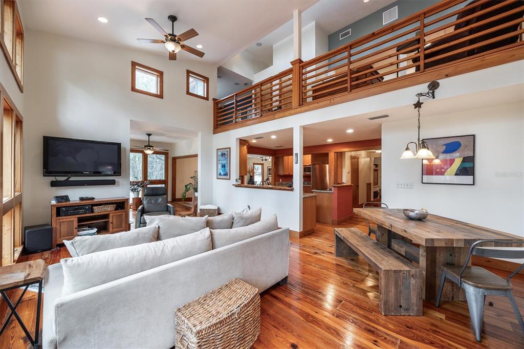 An open-concept living and dining area features hardwood floors, a loft balcony, and vaulted ceilings — 22675 NW 75TH AVENUE ROAD, MICANOPY, FL