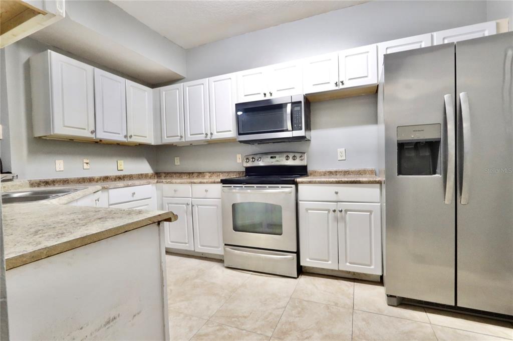 A kitchen features white cabinets, stainless steel appliances, and tan laminate countertops — 5578 METROWEST BOULEVARD UNIT 1-201, ORLANDO, FL