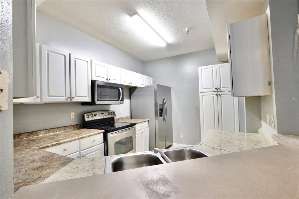 A kitchen features white cabinets, stainless steel appliances, and laminate countertops — 5578 METROWEST BOULEVARD UNIT 1-201, ORLANDO, FL