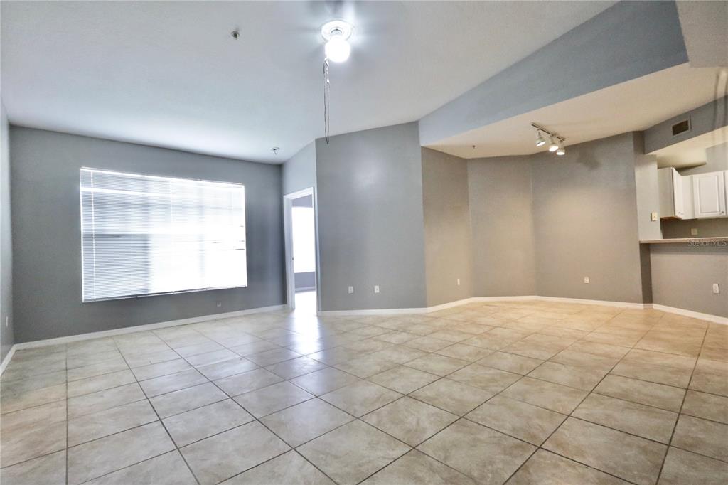 An open-concept living area features light gray walls, large windows with blinds, and beige tile flooring — 5578 METROWEST BOULEVARD UNIT 1-201, ORLANDO, FL