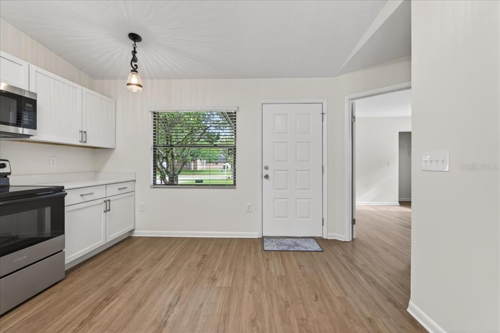 A kitchen with white cabinets, stainless steel appliances, and wood-look flooring near an exterior door — 10 BREN MAR LANE, PALM COAST, FL