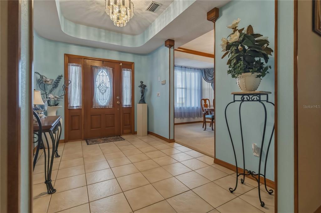 A tiled foyer features a wooden front door, a crystal chandelier, and light blue walls — 2620 TOUPS TRAIL, TITUSVILLE, FL