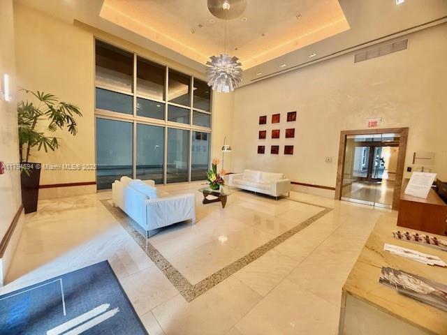 A bright, high-ceilinged lobby features white sofas, a modern chandelier, and large glass windows — 1050 Brickell Ave # 1602, Miami FL 33131, MIAMI, FL