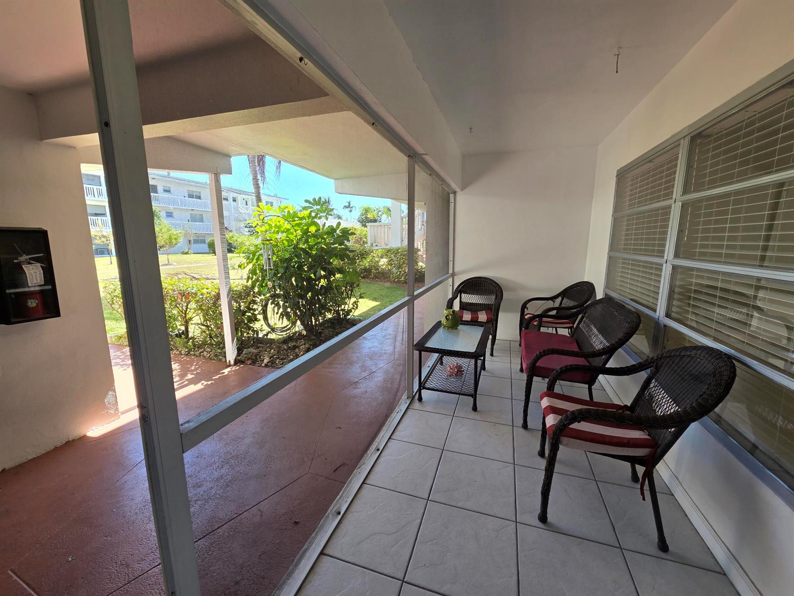 A screened-in patio features tiled flooring, wicker chairs with striped cushions, and a small table — 600 Pine Drive # 103, Pompano Beach FL 33060, POMPANO BEACH, FL