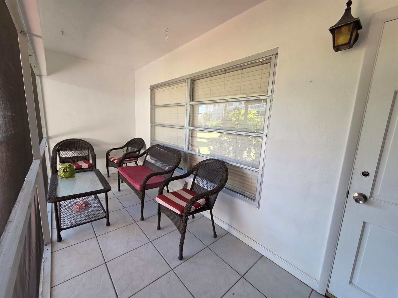 A screened-in porch features tiled flooring, wicker furniture, and a large window with blinds — 600 Pine Drive # 103, Pompano Beach FL 33060, POMPANO BEACH, FL