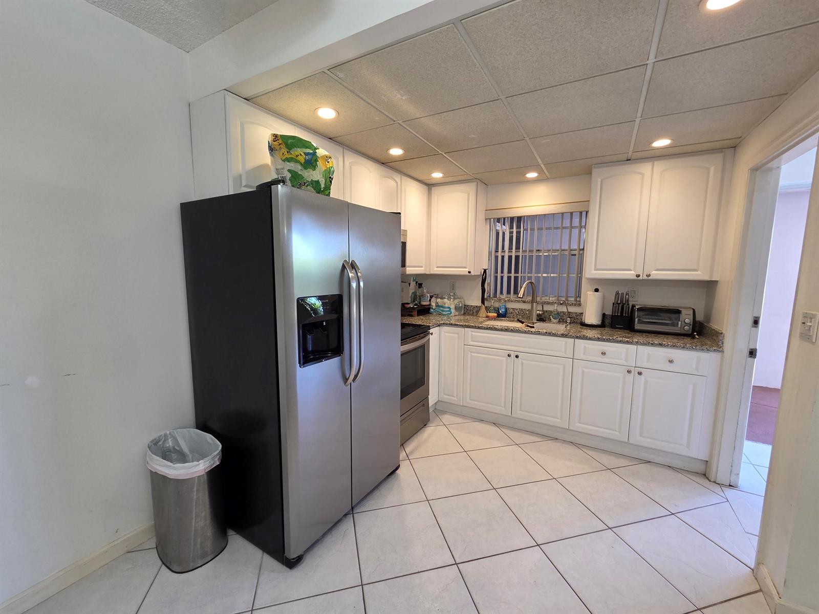 A kitchen features white cabinets, stainless steel appliances, granite countertops, and light-colored tile flooring — 600 Pine Drive # 103, Pompano Beach FL 33060, POMPANO BEACH, FL