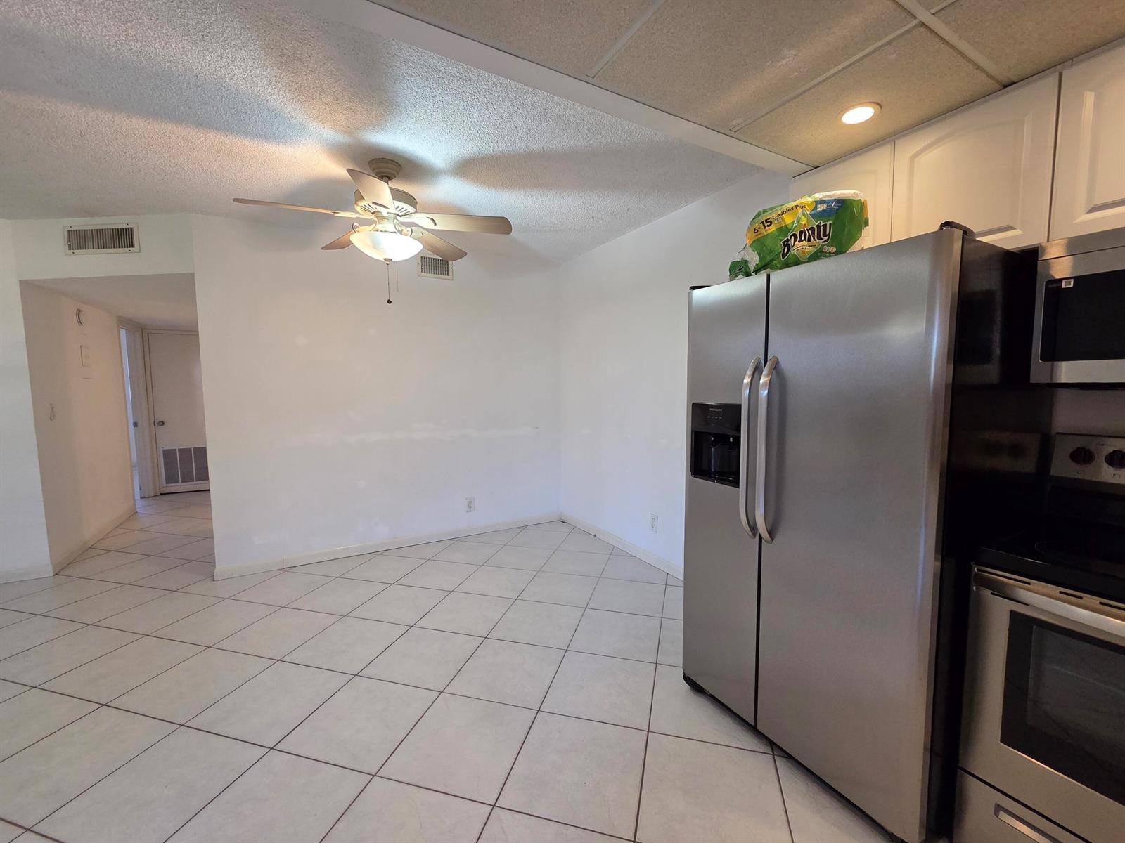 A kitchen with stainless steel appliances, white cabinets, and tile flooring opens to a dining area — 600 Pine Drive # 103, Pompano Beach FL 33060, POMPANO BEACH, FL