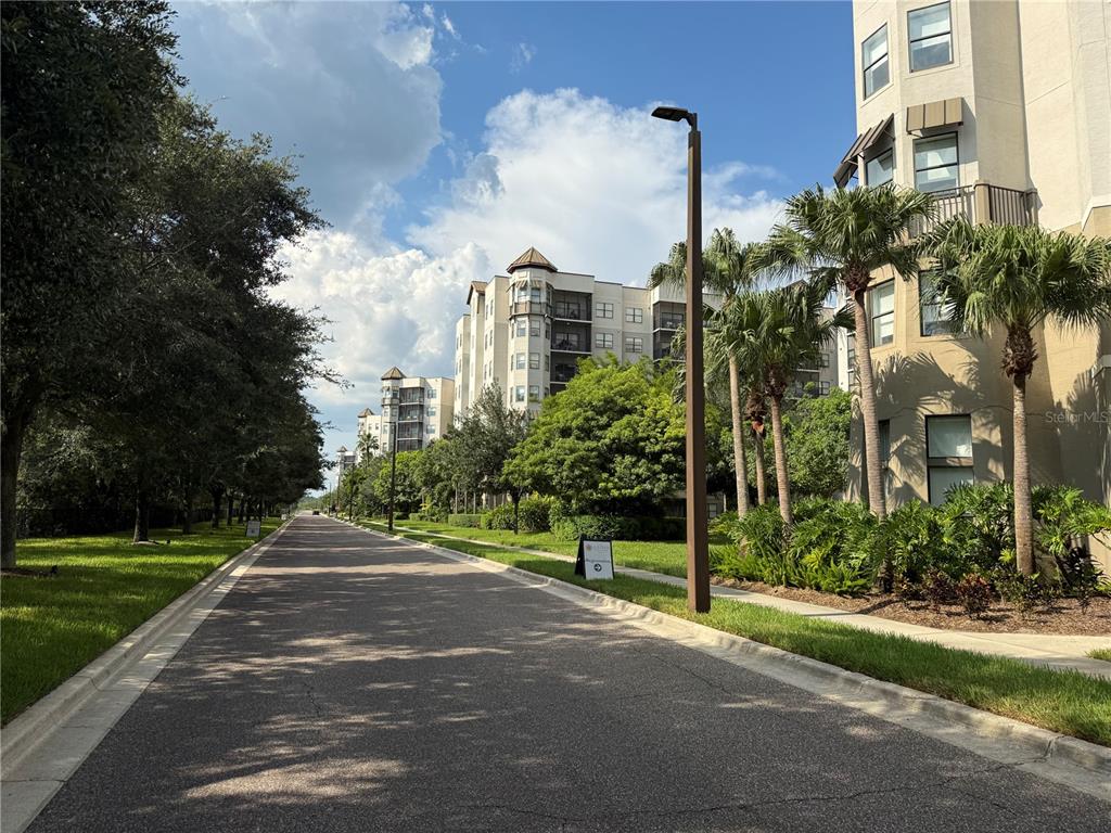 A paved road leads past multi-story apartment buildings and palm trees under a blue sky — 14501 GROVE RESORT AVENUE UNIT 1220, WINTER GARDEN, FL