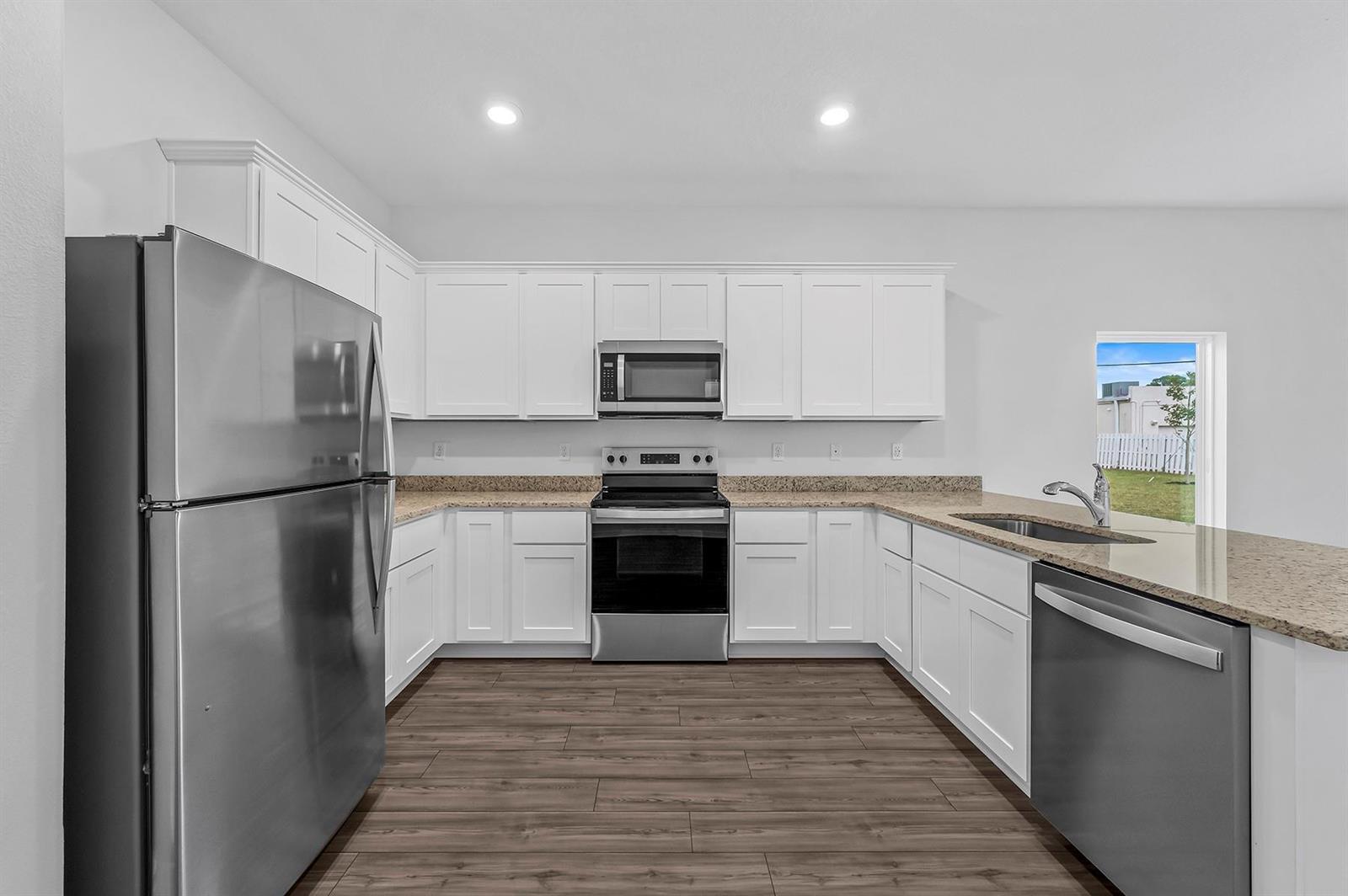 A kitchen with white cabinets, stainless steel appliances, granite countertops, and wood-look flooring — 5604 Sunset Boulevard, Fort Pierce FL 34982, FORT PIERCE, FL