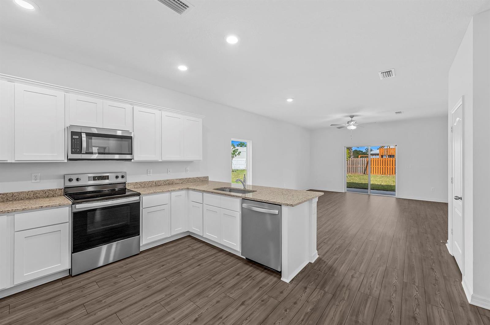 A kitchen with white cabinets, granite countertops, and stainless steel appliances opens to a living area — 5604 Sunset Boulevard, Fort Pierce FL 34982, FORT PIERCE, FL