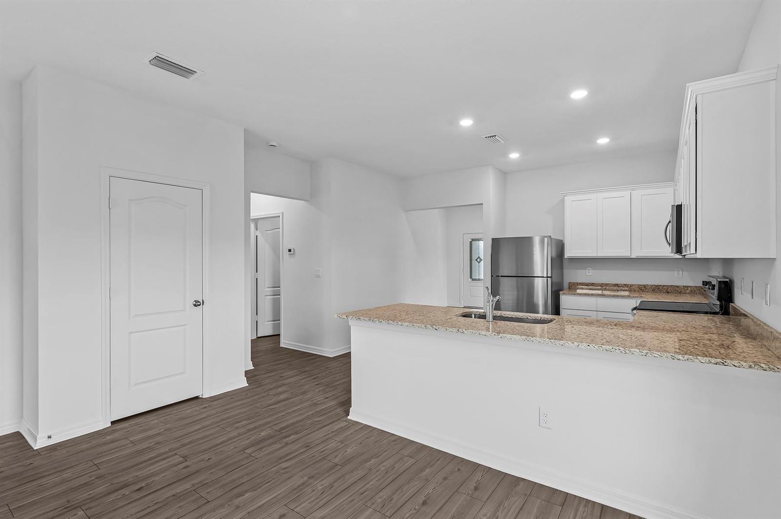 A kitchen with white cabinets, granite countertops, stainless steel appliances, and wood-look flooring — 5604 Sunset Boulevard, Fort Pierce FL 34982, FORT PIERCE, FL