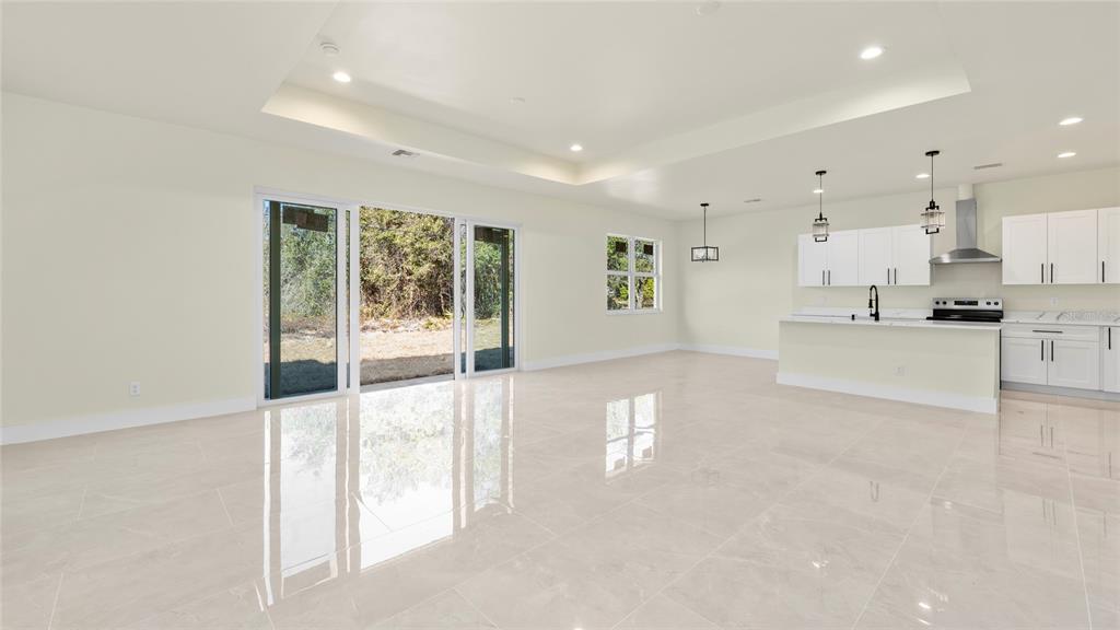 A bright, open-concept living and kitchen area features white cabinetry, tile flooring, and sliding doors — 1359 SULSTONE DRIVE, PUNTA GORDA, FL