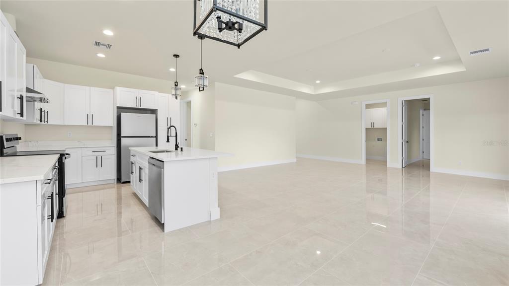 A modern kitchen with white cabinetry and a central island opens into a spacious room — 1359 SULSTONE DRIVE, PUNTA GORDA, FL