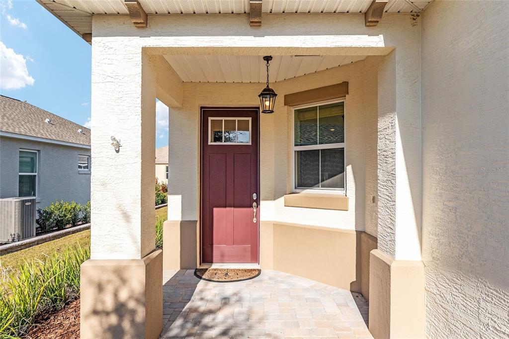 A covered entryway features a red front door, a pendant light, and stone pavers — 9698 SW 103RD TERRACE, OCALA, FL