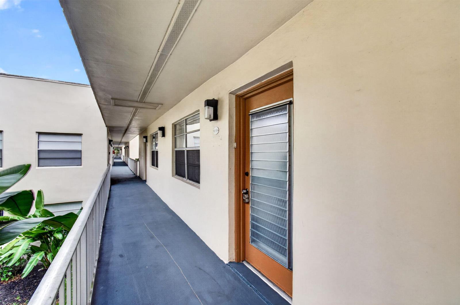 An exterior walkway leads past apartment doors with louvered glass inserts and windows — 190 Piedmont D, Delray Beach FL 33484, DELRAY BEACH, FL
