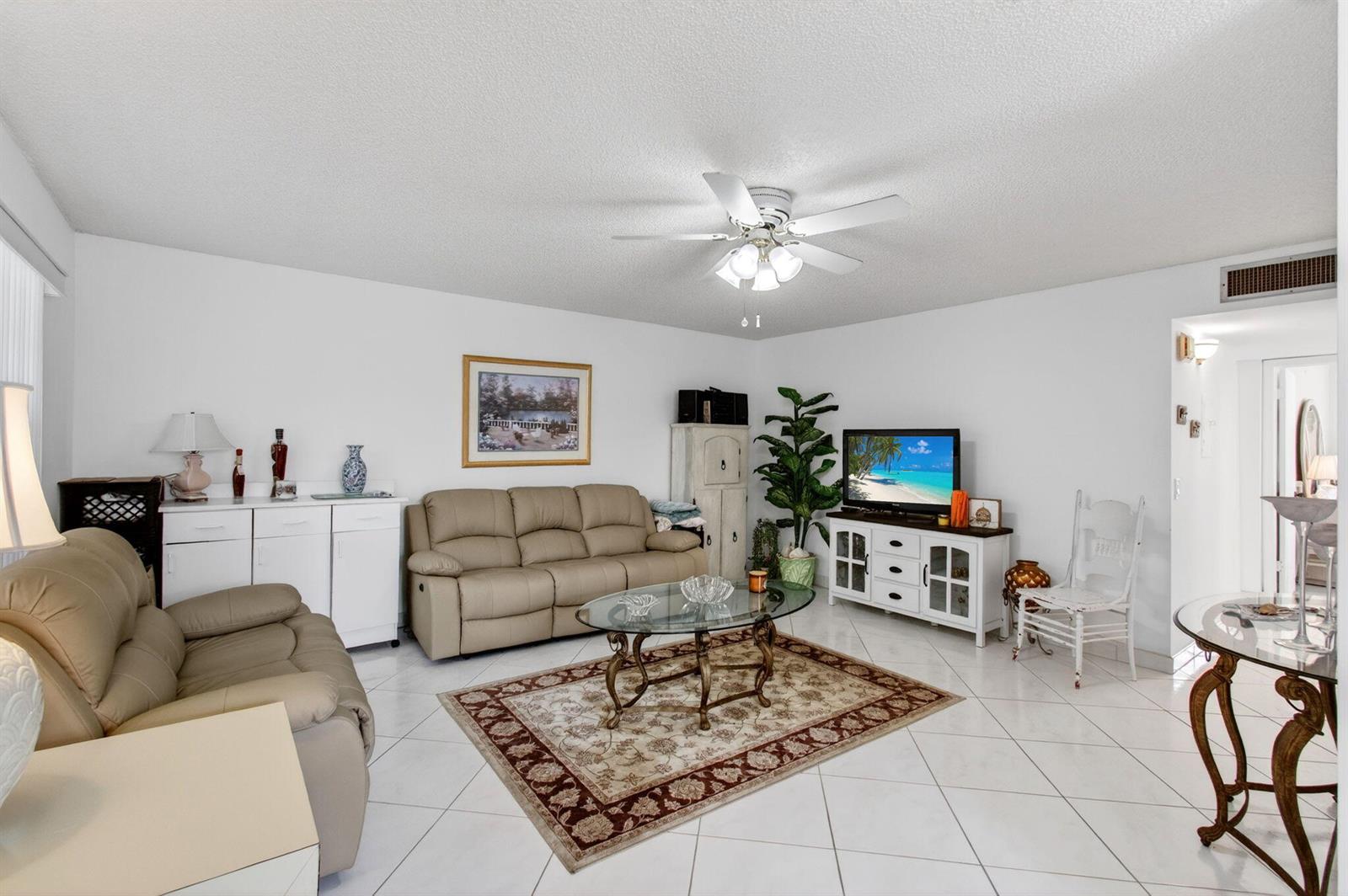 A living room features white tile floors, a tan sofa, a glass coffee table, and a television — 190 Piedmont D, Delray Beach FL 33484, DELRAY BEACH, FL