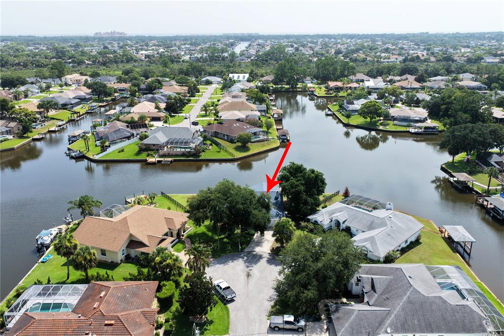An aerial view shows a waterfront house with a red arrow pointing toward its roof — 23 COMMANDER COURT, PALM COAST, FL