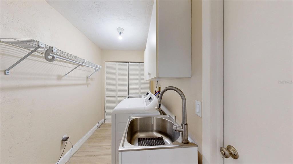 A laundry room features a utility sink, white cabinetry, a wire shelf, and a washer — 23 COMMANDER COURT, PALM COAST, FL